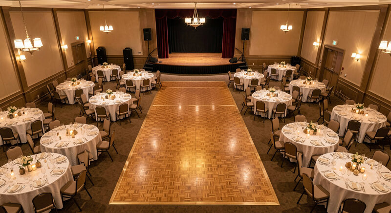 An overhead view of a banquet room with round tables, a clear parquet dance floor and a small stage at the far end.